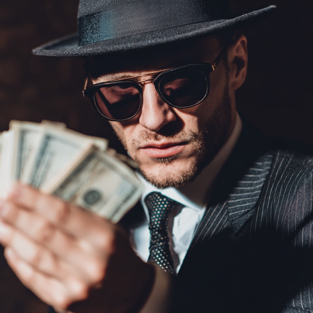Celebrity impersonation scams target victims - sophisticated scammer wearing suit and sunglasses holding money representing how criminals exploit parasocial relationships with fake celebrity profiles for financial gain